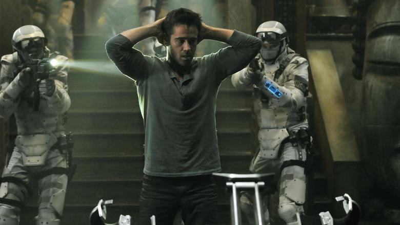 Colin Farrell surrounded by armed soldiers with his hands behind his head in Total Recall