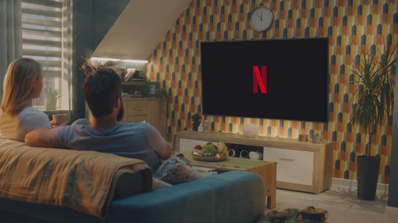 two people sitting on a couch watching a black screen with the Netflix logo on it