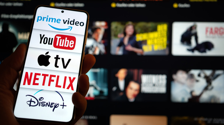 A list of streaming platforms on a phone in front of a TV