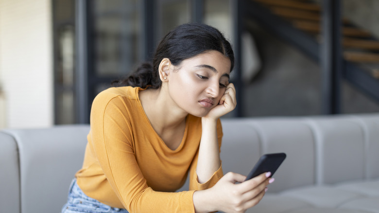 Woman sitting on couch looking at phone with bored expression