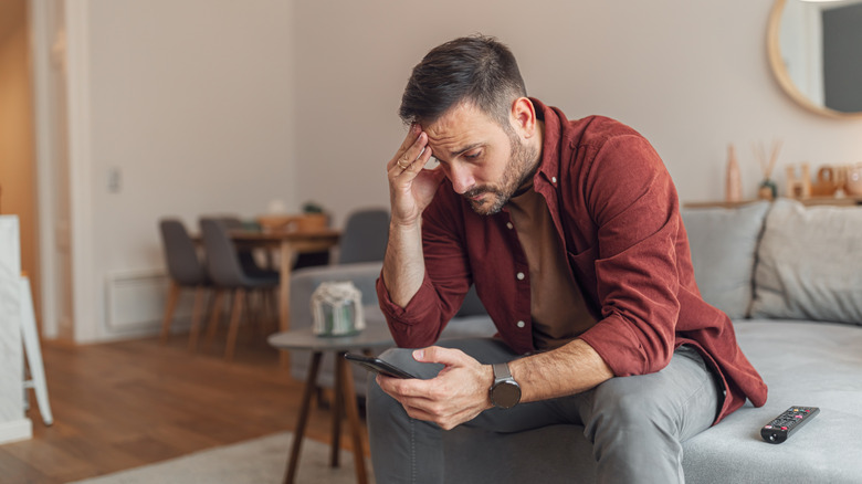 Person sitting on couch and looking at phone with frustrated expression