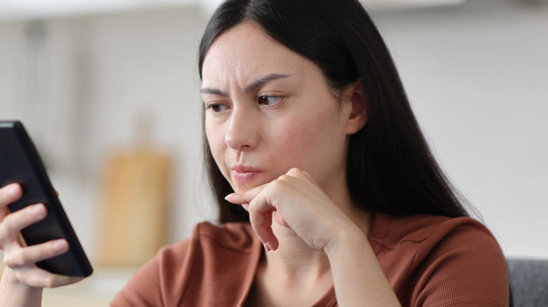 Woman looking at phone screen with mildly frustrated expression