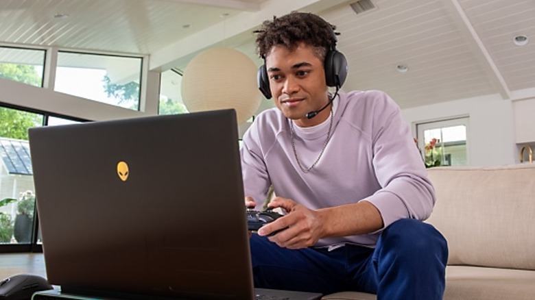 A person playing a game with headphones and a controller on an Alienware x14 R2 gaming laptop
