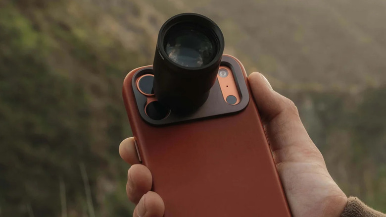 A hand holds an iPhone in a leather case with Sandmarc's new tetraprism lens.