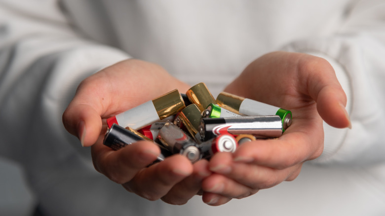 Two hands holding a bunch of batteries.