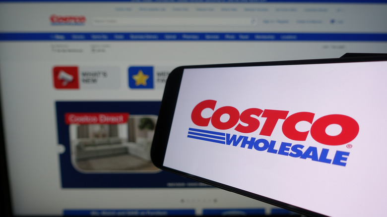 The Costco logo on a smartphone screen held in front of a PC web browser
