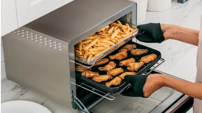 Person taking out baked chicken wings and French fries from the Smart Air Fryer Oven