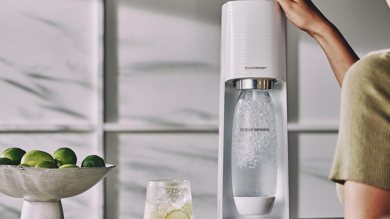Person clicking the top of the SodaStream to carbonate the water container