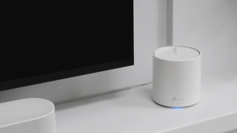 TP-Link Deco mesh router sitting next to a television screen and on a counter
