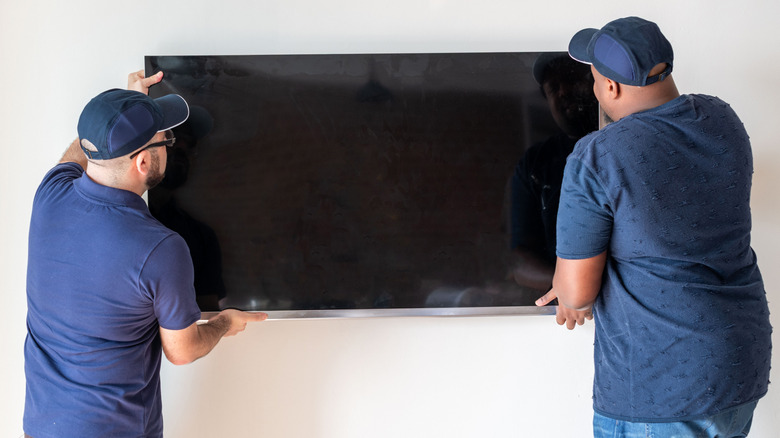 Two people installing TV on a wall