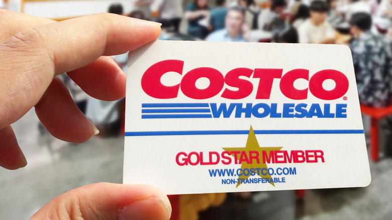 A hand holding up a Costco gold star membership card inside the store