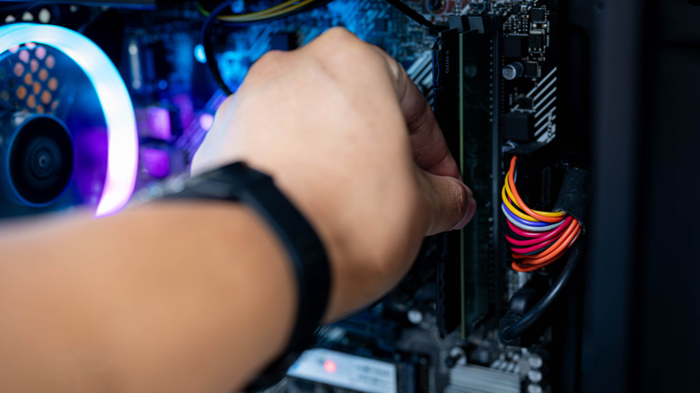 Hand installing a RAM module into a desktop PC motherboard with RGB fan lighting