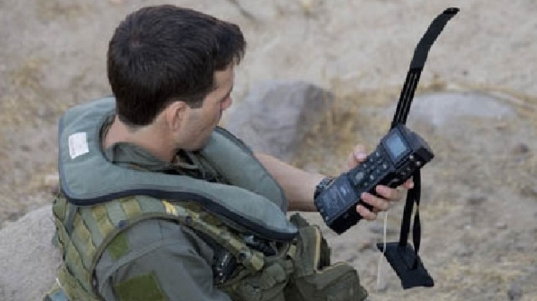 A soldier sits in a desert area, holding his handheld CSEL system