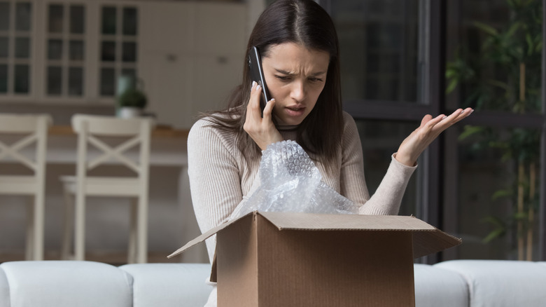 an upset woman on the phone looking into an opened box