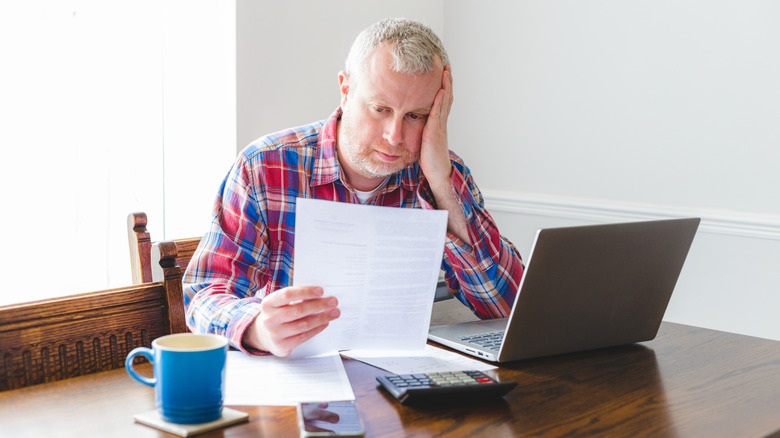 A man reviewing bills beside a laptop and calculator.