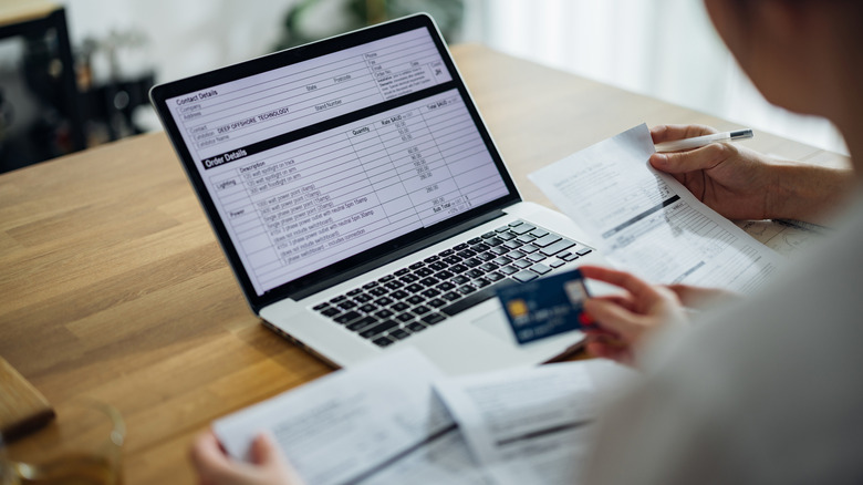 A person reviewing billing details on a laptop while holding a credit card.