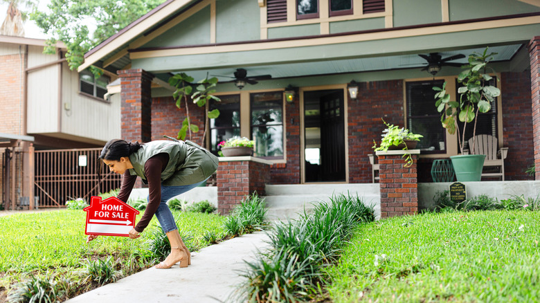 A woman setting up a home for sale sign in a yard