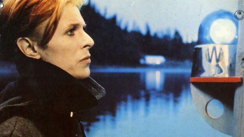 Thomas (David Bowie) standing next to a river in 