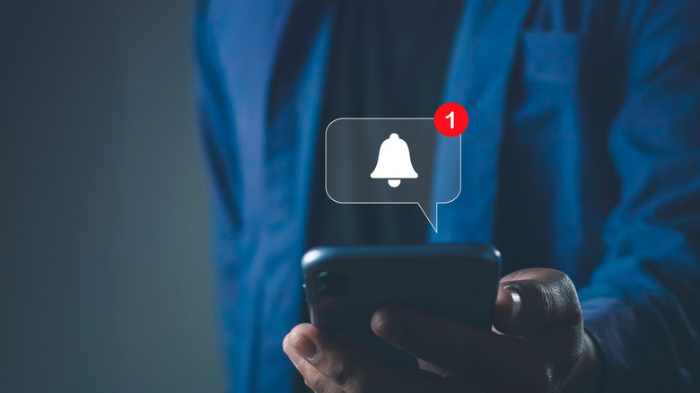 A hand holding a phone, with a conceptual rendering of an app alert in a thought bubble above the phone