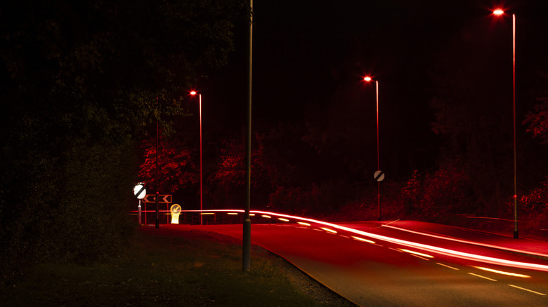 A road at night lit up by red streetlights featuring a long exposure trail of red light from a car.