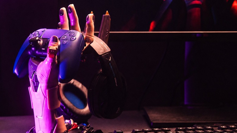 The Grupo Erik Cyborg Hand Stand holding black headphones and a black game controller.