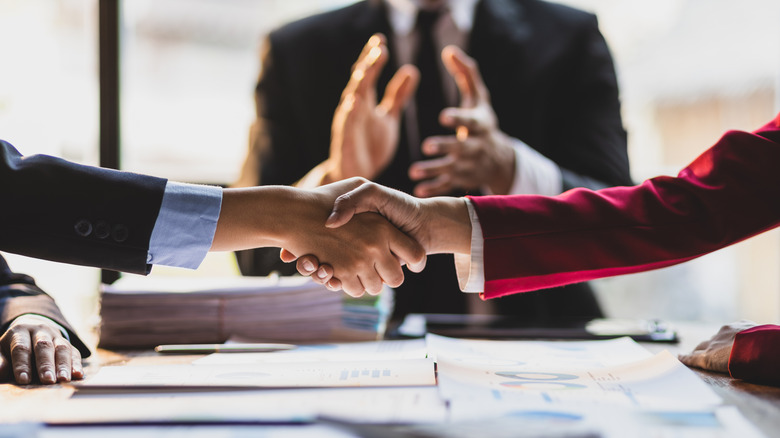 Business people making a deal and shaking hands with a person clapping in the background