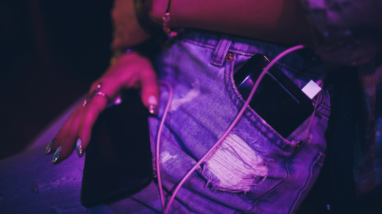 a woman charging her phone with a portable charger in her pocket