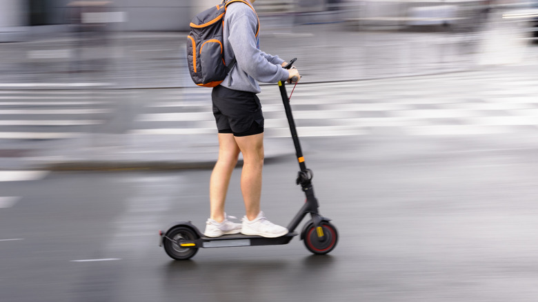 A person riding an electric scooter and wearing a backpack against a blurred cityscape.
