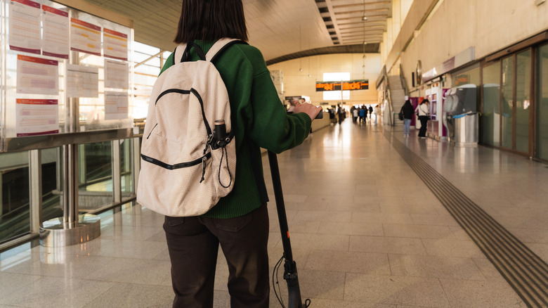 A person with an electric scooter and wearing a backpack in an airport.
