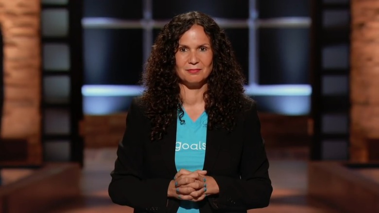 Tanya Van Court pitching Goalsetter on Shark Tank. She has long curly hair and is wearing a black blazer and blue t-shirt.