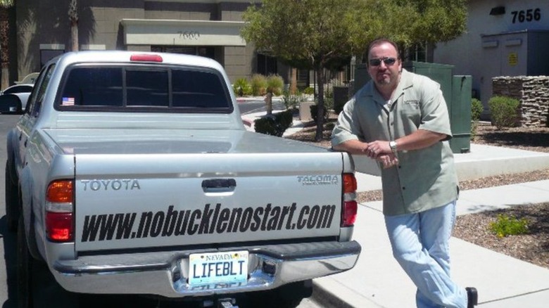 Lifebelt founder Robert Allison leaning on a gray truck that has www.nobucklenostart.com on the back and a 