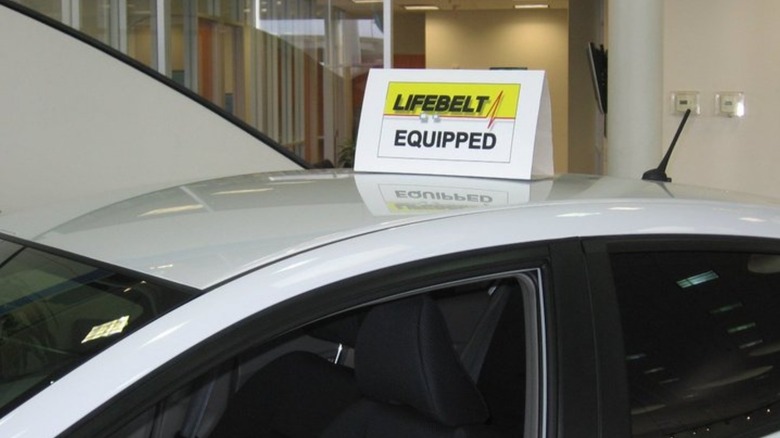 A white car with a sign that says "Lifebelt Equipped" placed on top