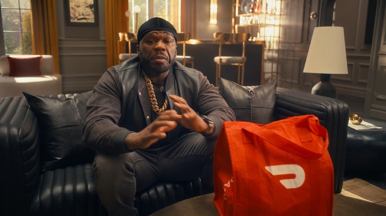50 Cent on a couch with a red DoorDash bag on the table in front of him