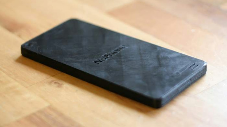 A black piece of plastic with "NoPhone" etched into the center. It sits on a hardwood surface.