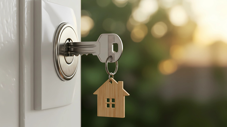 A house key in a front door, with a keychain in the shape of a cutout house