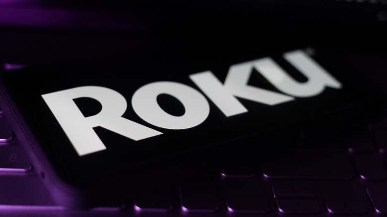 An iPhone showing the word "Roku" on a dark purple background.