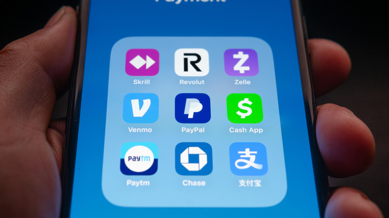 Person holding an iPhone displaying various digital payment apps