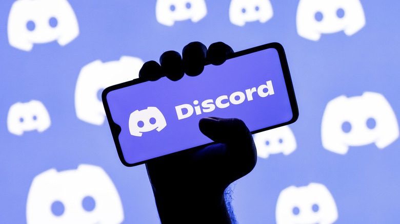 An individiual's right hand holding a cellphone that's displaying the Discord logo, the logo is also patterned in the background