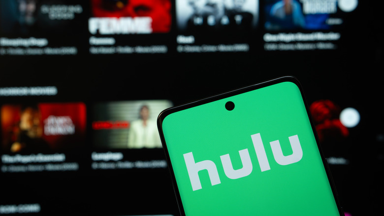 smartphone with hulu logo in front of a tv showing streaming library