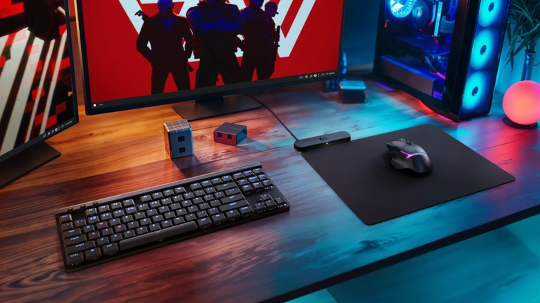 Logitech mouse, mousepad, and keyboard on a wooden desk in front of a gaming PC