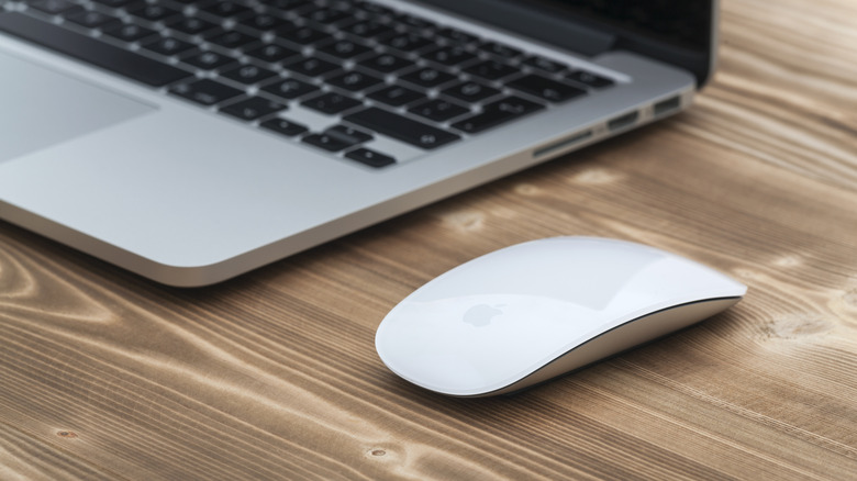 An Apple Magic Mouse with an out of focus MacBook Pro in the background