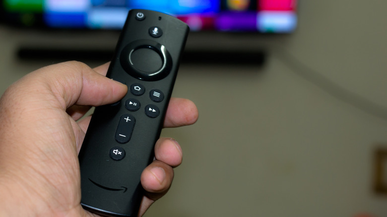 Hand holding Amazon Fire TV remote and pointing at TV