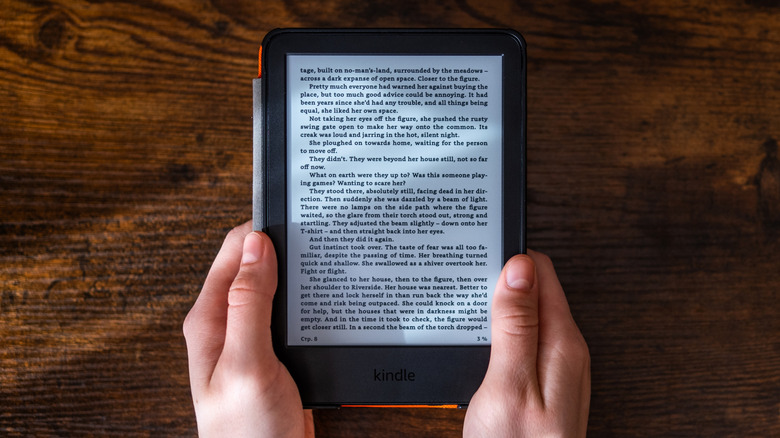 Person holding a Kindle e-reader displaying an ebook page over a wooden table.