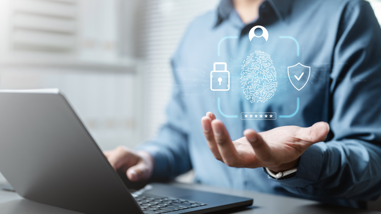 A person holding hand under a hologram of a digital fingerprint security symbol next to a laptop
