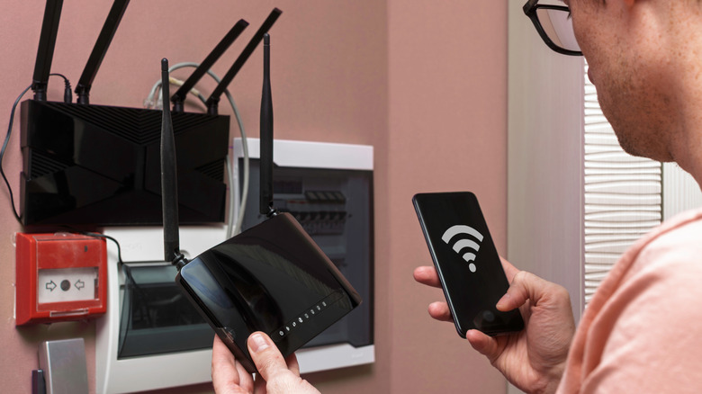Man configuring Wi-Fi router and extender with lots of antennas visible.
