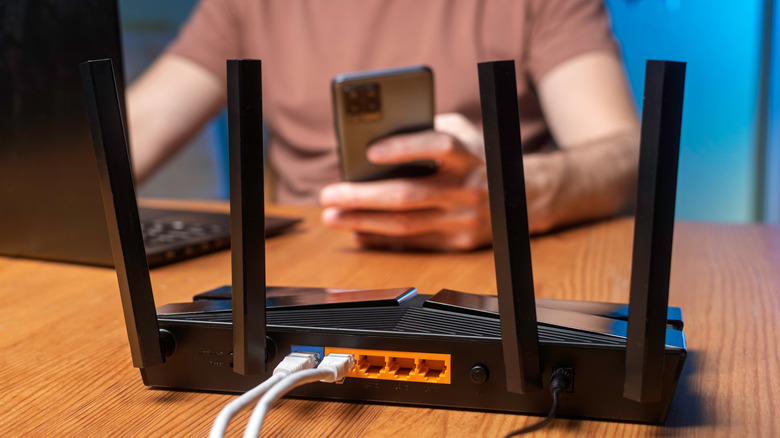 Close up of Wi-Fi router with antennas upright and user in background.