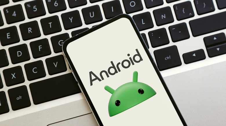 A phone with the Android logo on its screen, resting on top of a laptop keyboard