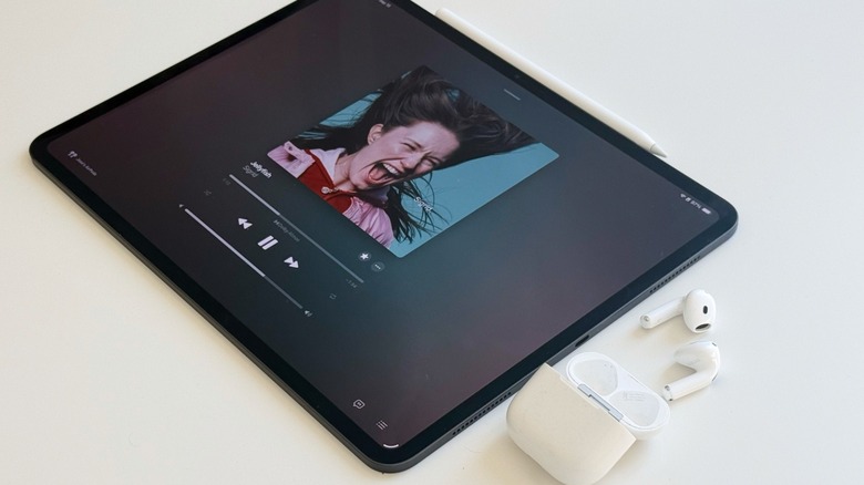 A pair of white AirPods 4 beside a black iPad Pro.