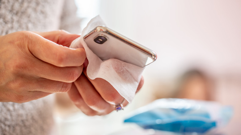Close up of hands cleaning a smartphone with a wipe.
