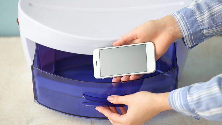 Close up of hands putting a smartphone into the drawer of a UV phone sanitizer machine